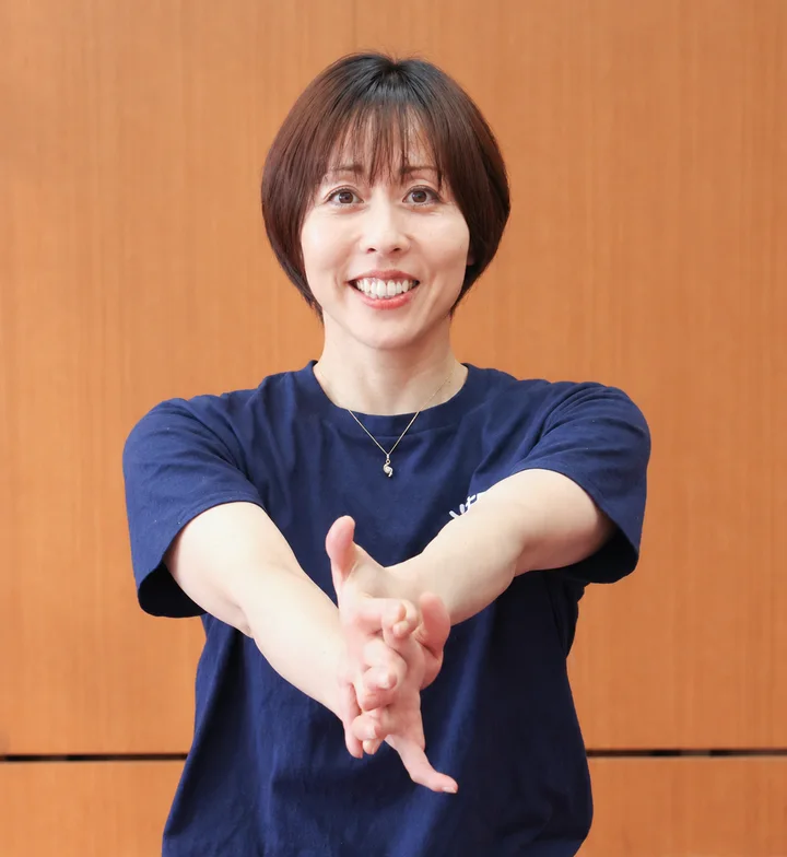 両手を前に伸ばしてOSTEO®の体操のポーズをとる、OSTEO® PERSONAL担当の広島大学准教授 黒坂志穂